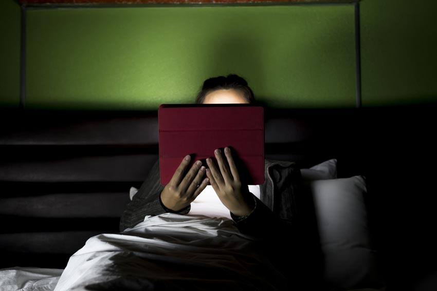 A person reading with a tablet on the bed at night