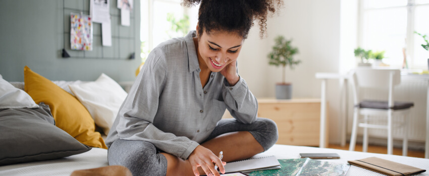 smiling woman sitting on her bed looking at her notebooks