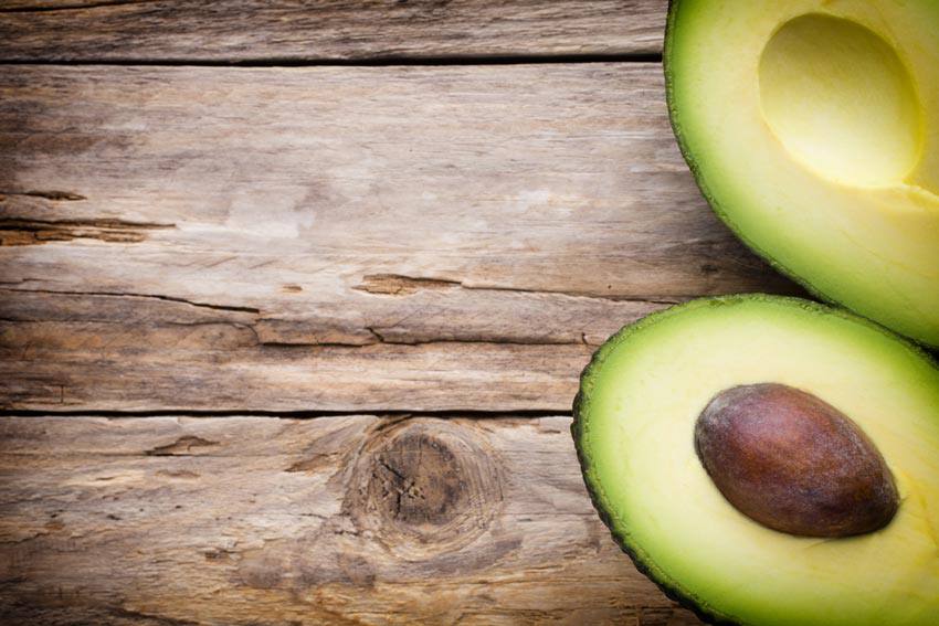 An avocado split in two resting on a wooden table